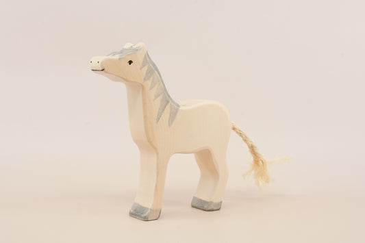 Hand-carved wooden toy horse in a natural light wood finish with painted gray details on the mane, hooves, and face, and a braided straw tail, shown against a plain light beige background.