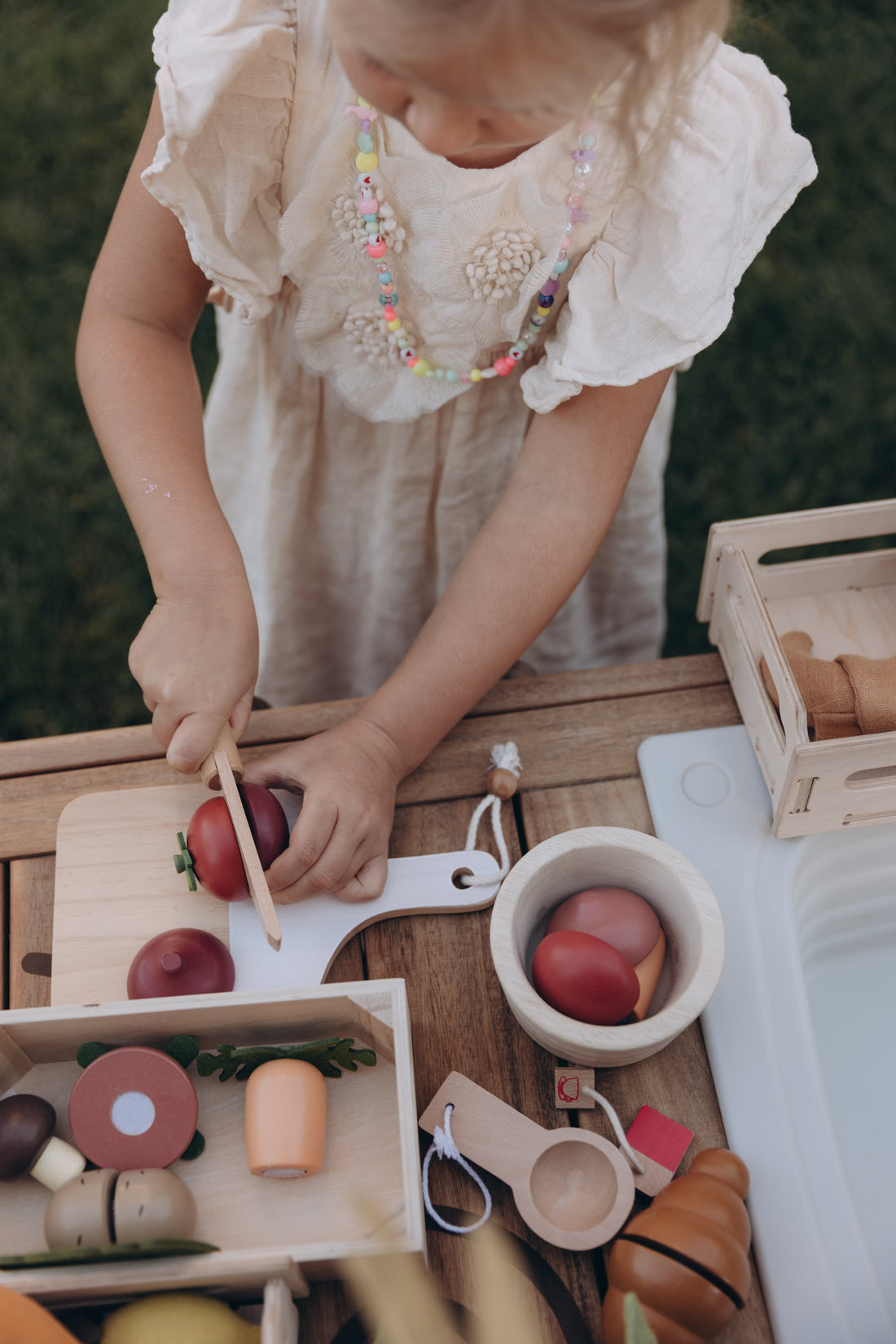 Toddler slicing wooden play food vegetables with a toy knife during imaginative kitchen play