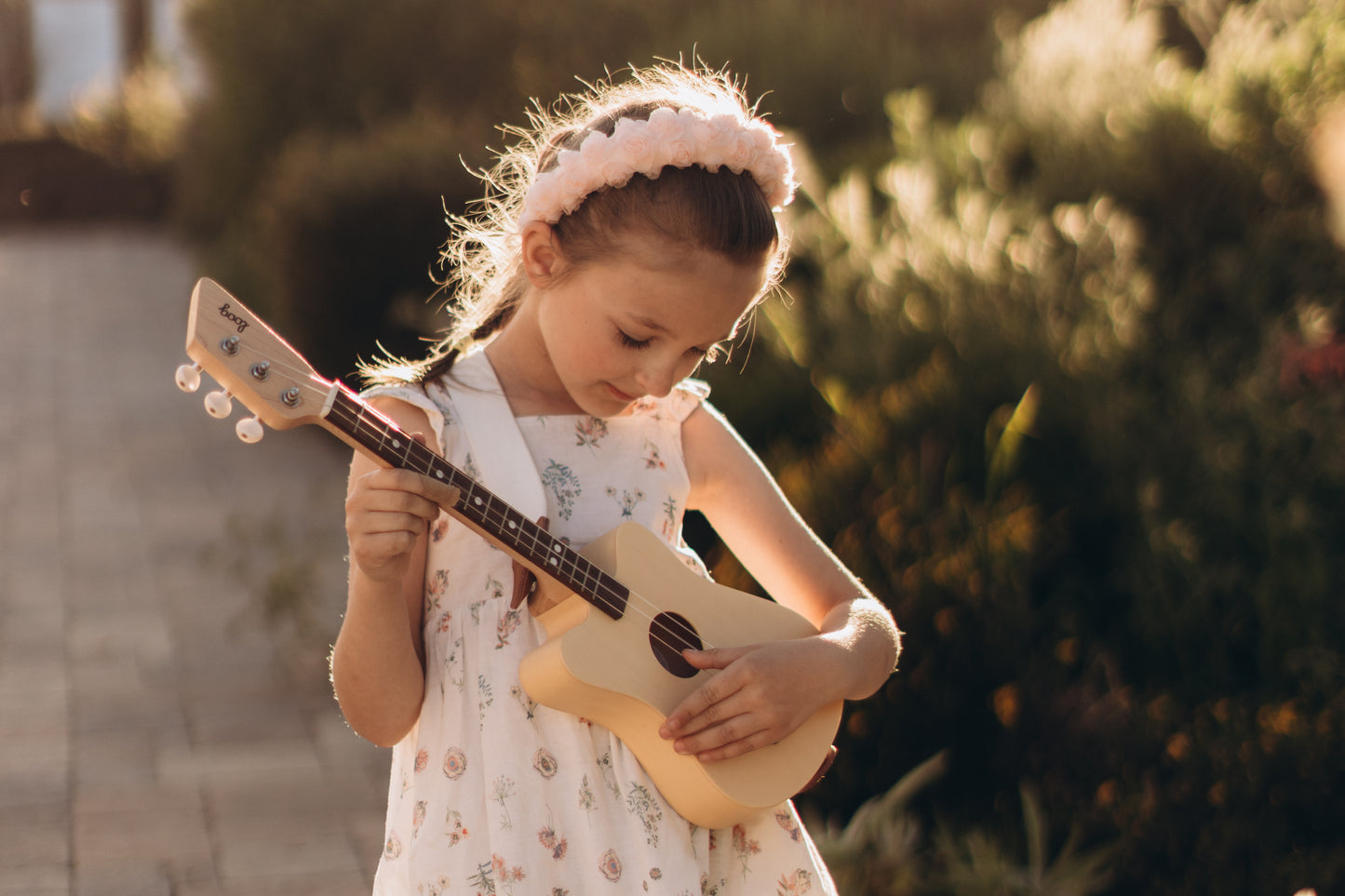 Young girl playing a small guitar outdoors with greenery in the background