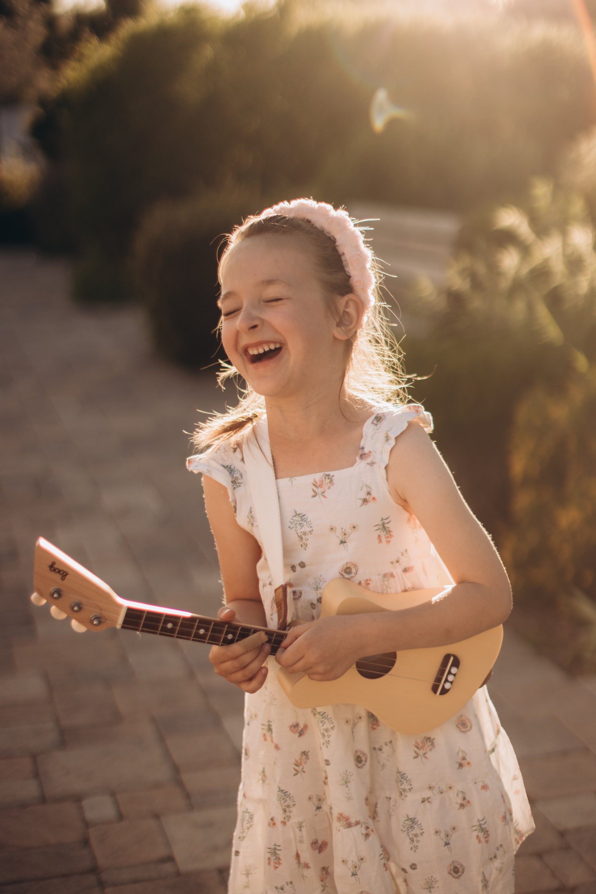 Young girl playing a ukulele outdoors with sunlight filtering through.