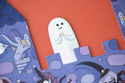 A close-up of a Halloween-themed jigsaw puzzle showing a white ghost character with a gold star, set against a bright orange background and purple castle pieces with cartoon cat and witch illustrations.